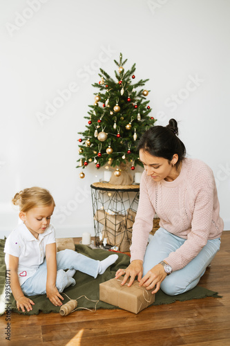 Mom and daughter  packing Christmas gifts in room. Merry christmas and happy new year concept. Space for text. Family cozy moments.Morning before Xmas.. photo