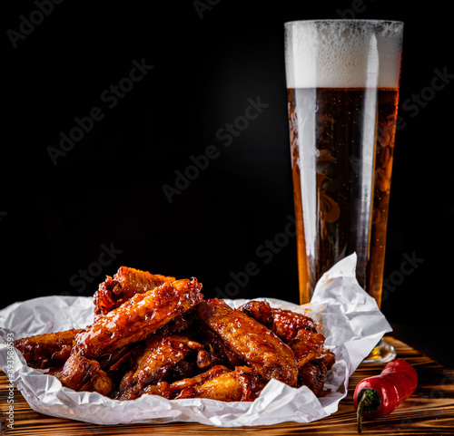Canvas Print glass of fresh beer and fried chicken wings on wooden table on black background
