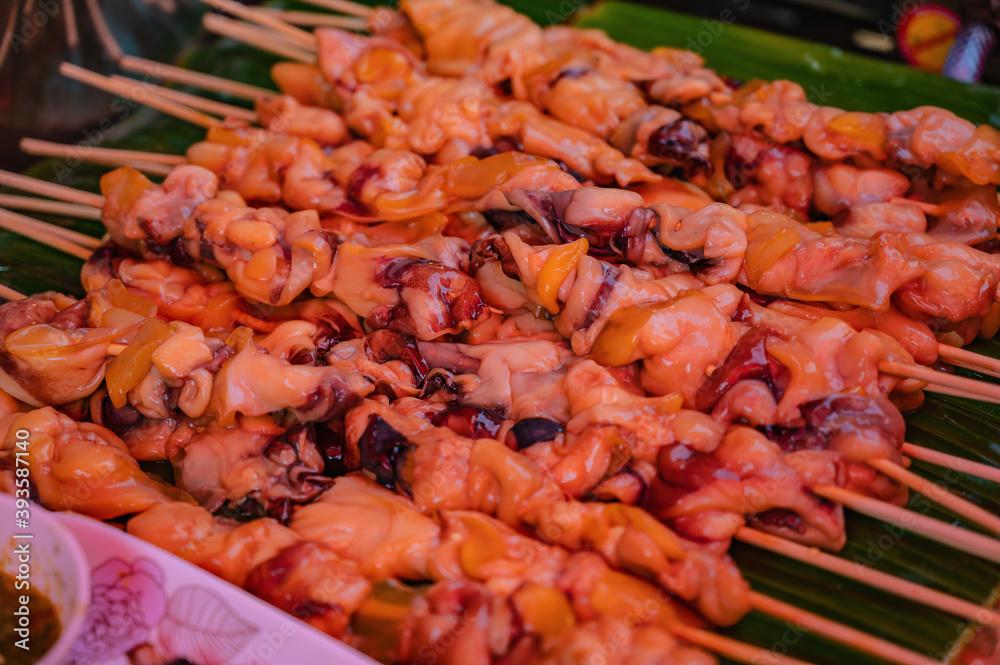 Close up raw squid meat skewer on banana leaf in the fresh market of thailand with spicy seafood sauce.Thailand street food