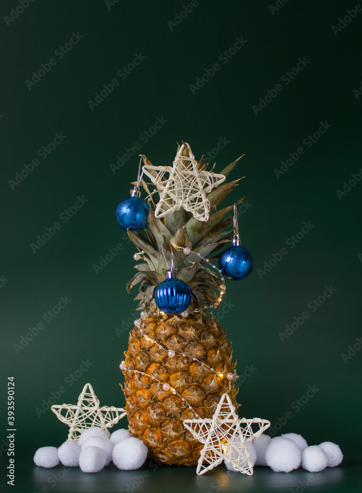 Christmas decor concept with pineapple, balls, stars and artificial snowballs on green background. Vertical. Copy space
