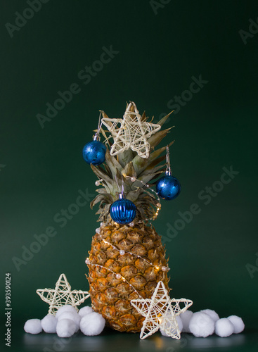Christmas decor concept with pineapple, balls, stars and artificial snowballs on green background. Vertical. Copy space © DiandraNina