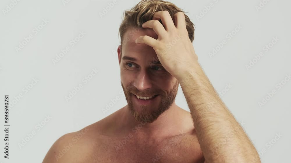 A pleased blonde man is posing to the camera standing isolated over a grey background in the studio