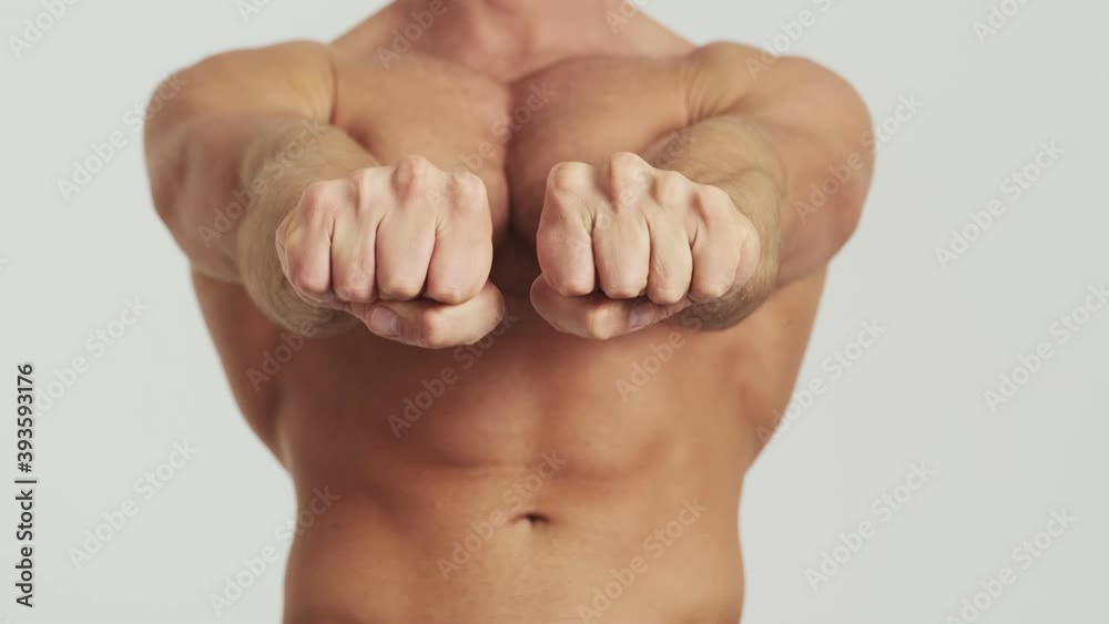 A cropped-view of a half-naked man is showing his torso muscles posing to the camera standing isolated over a grey background in the studio A cropped-view of a half-naked man is showing his torso muscles posing to the camera standing isolated over a grey background in the studio