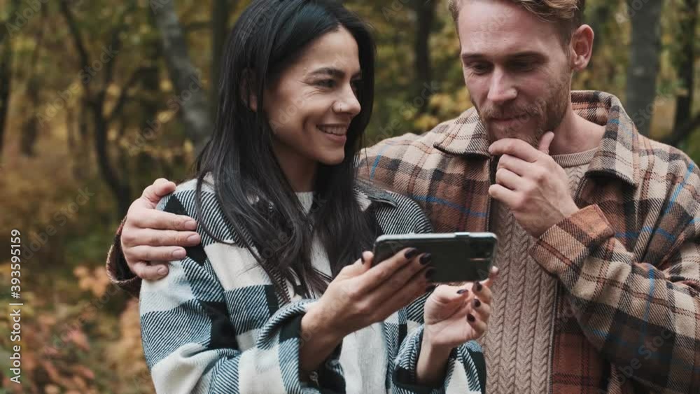 A beautiful couple man and woman are watching something in the smartphone while walking in the autumn park A beautiful couple man and woman are watching something in the smartphone while walking in the autumn park