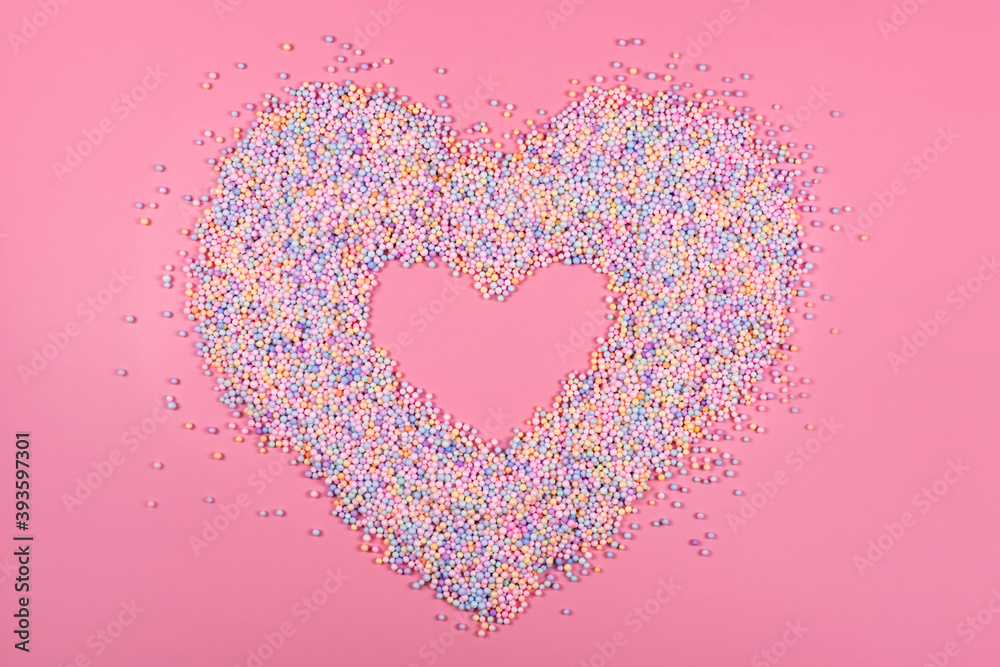 Heart frame made of pastel color balls on pink. Styrofoam or Polystyrene foam background. Mixed colorful sugar balls for sweets decoration. Rainbow sugar candies, dragee, confectionery. Love concept