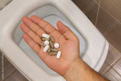 Male hand with medical diarrhea tablets over toilet photo