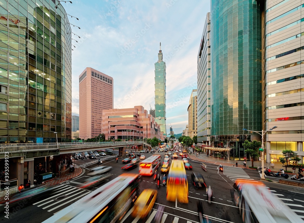 Obraz premium View of a busy street corner in Downtown Taipei City at rush hour with cars & buses dashing by, Taipei 101 Tower & World Trade Center Building in Xinyi Financial District & people passing on crosswalk