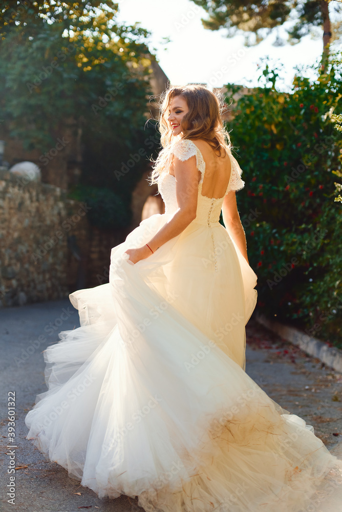 Beautiful stylish bride in a white dress. Posing against the backdrop of green bushes. Beautiful backlight