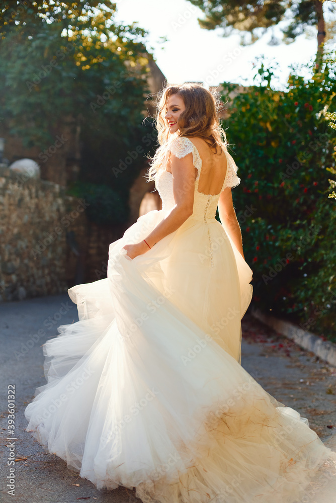 Beautiful stylish bride in a white dress. Posing against the backdrop of green bushes. Beautiful backlight Beautiful stylish bride in a white dress. Posing against the backdrop of green bushes. Beautiful backlight