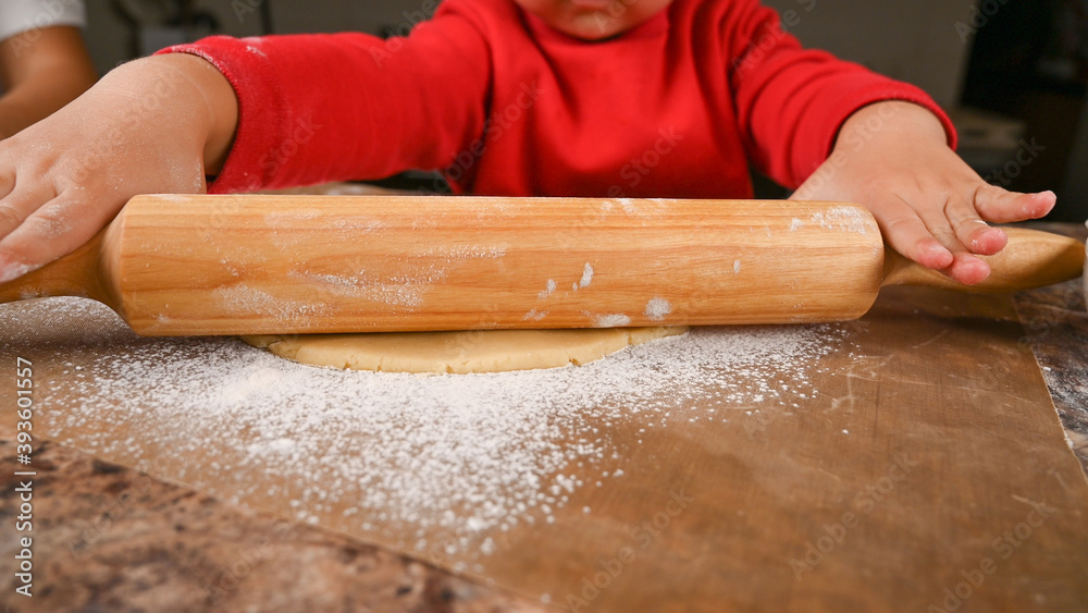 The child learns to roll the dough with a rolling pin The child learns to roll the dough with a rolling pin