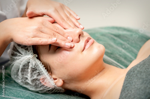 Young woman getting facial massage with closed eyes by beautician in beauty salon