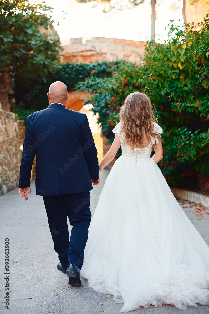 The newlyweds walk and smile, at the entrance to the castle against the background of a stone wall and palm trees. The newlyweds walk and smile, at the entrance to the castle against the background of a stone wall and palm trees.