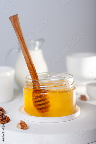 Flower honey in glass bowl with wooden dipper, milk and dishes on a white table