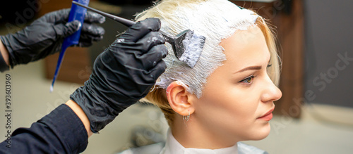 Hand of hairdresser applying white paint to client's hair in barbershop