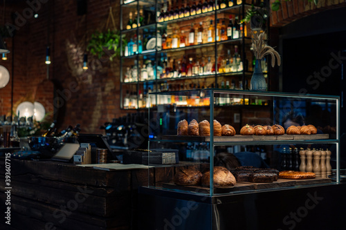 Bar counter with a pastry showcase in small restaurant. Bottles Of Alcohol And Spirits On Backlight Shelves on background. Image with selective focus