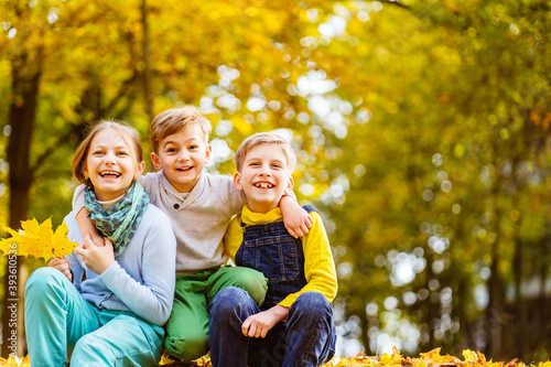 Portrait of three children of different age spending time together at autumn time by a forest or park looking at camera laughing. Positive emotions, enjoy childhood concept.