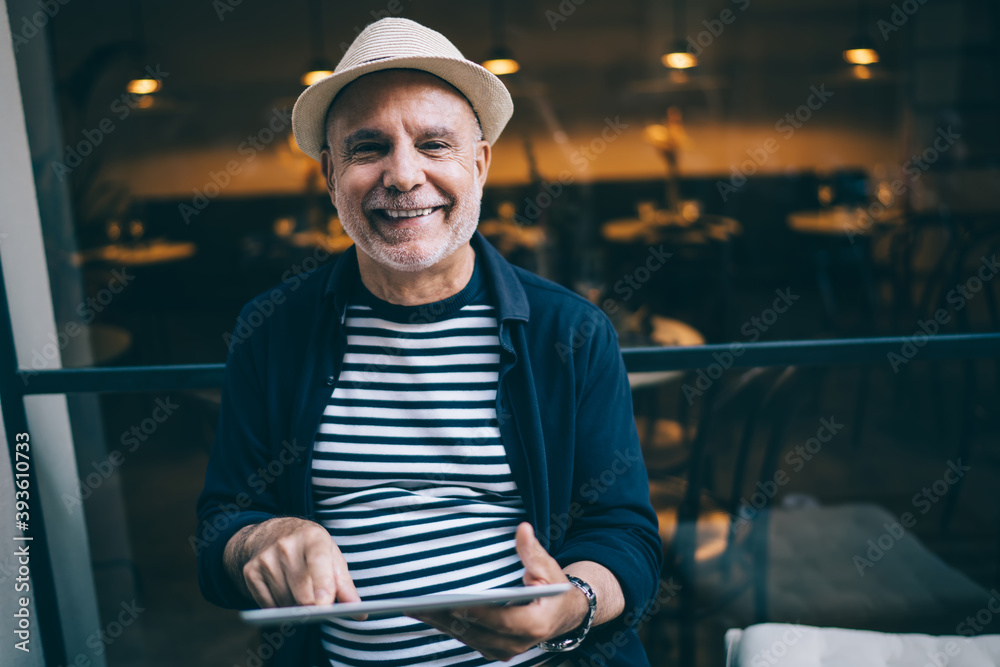 Portrait of happy Caucaisan blogger on retirement holding digital tablet in hands and smiling at camera during rest daytime in city, cheerful male senior in straw hat using touch pad on leisure Portrait of happy Caucaisan blogger on retirement holding digital tablet in hands and smiling at camera during rest daytime in city, cheerful male senior in straw hat using touch pad on leisure