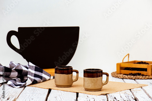 Dos tazas de café rústico, una caja de madera con granos de café, silueta negra de una taza de café sobre fondo blanco, con espacio para escribir.