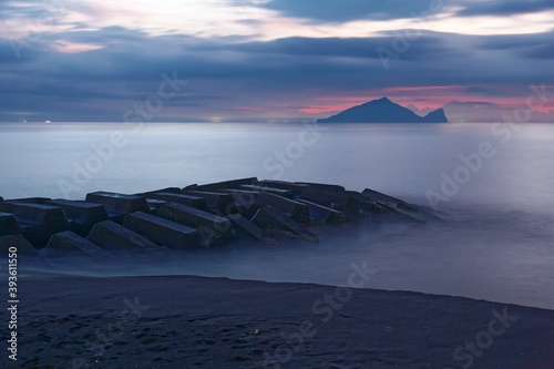 Beautiful scenery of a rocky beach in northern Taiwan on a foggy cloudy morning with a breakwater ( wave breaker ) in foreground & Guishan (Turtle) Island on distant horizon under dramatic dawning sky photo