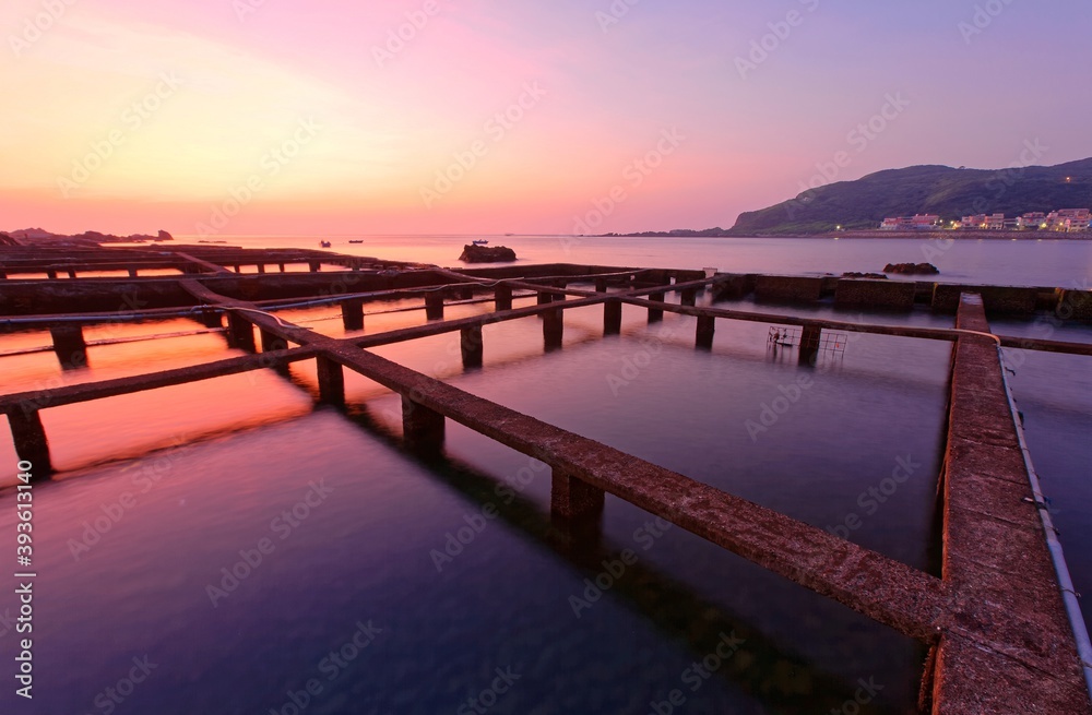 Obraz premium Beautiful sunrise scenery of a marine ranch (fish farming) in northern Taiwan, with peculiar artificial structures of aquaculture, fishing boats & islands on distant horizon under dramatic dawning sky