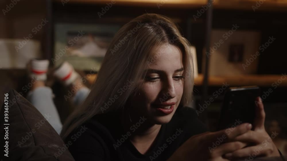 Beautiful sweet blonde woman lying on sofa and chatting with her phone in hand, lifestyle and social media concept
