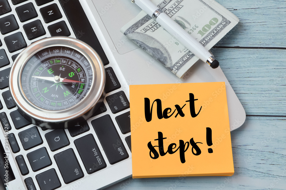 Selective focus of laptop, compass, banknote, pen and memo note written with NEXT STEPS!. Business concept. Selective focus of laptop, compass, banknote, pen and memo note written with NEXT STEPS!. Business concept.
