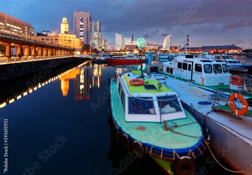 Vibrant night scenery of Yokohama Minatomirai Bay Area with boats and ships parking in the marina, colorful lights of a giant Ferris wheel and Landmark Tower among skyscrapers in the background