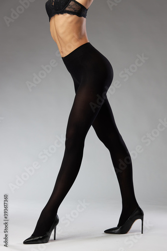 advertising shooting of nylon tights on a model in the studio on a gray background, she is wearing black tights and black heels (ID: 393617360)