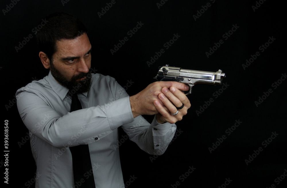 A handsome bearded man on isolated black background holds a gun in his hand pointing it in front of him. Gangster, policeman A handsome bearded man on isolated black background holds a gun in his hand pointing it in front of him. Gangster, policeman