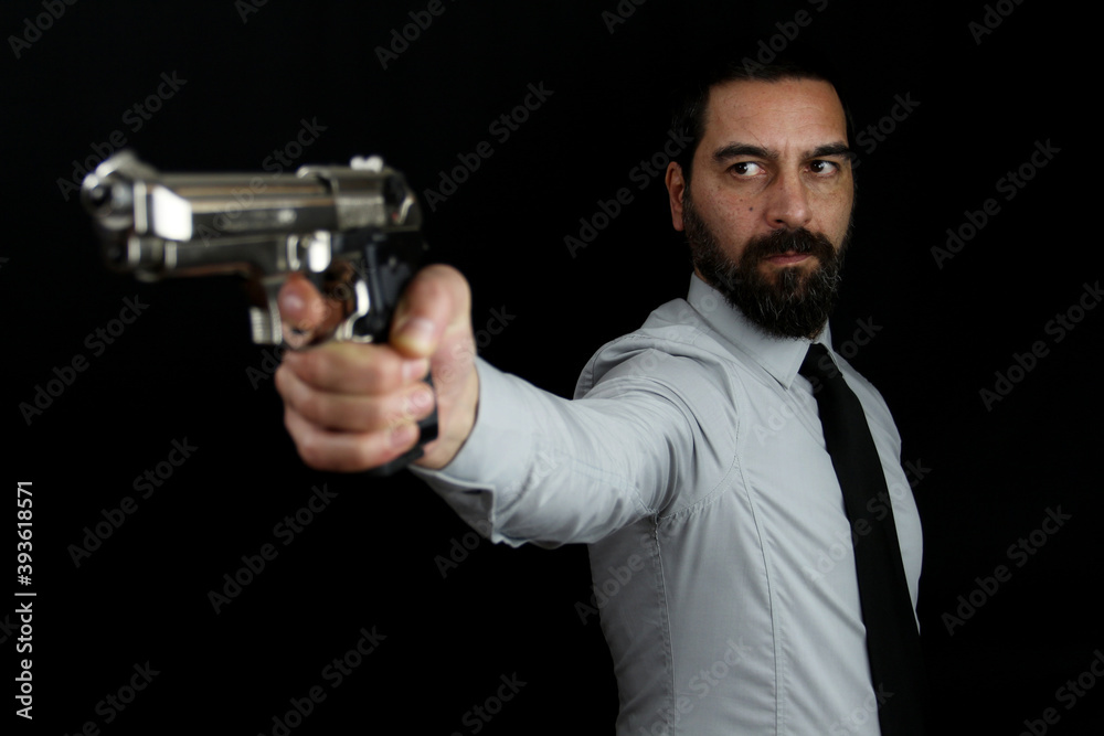 A handsome bearded man on black background holds a gun in his hand pointing it in front of him. Gangster, policeman A handsome bearded man on black background holds a gun in his hand pointing it in front of him. Gangster, policeman