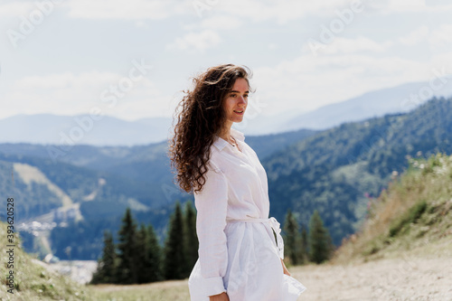 Girl traveler is smiling in the mountains. Attractive woman posing on the green hills background. Advert for travel agency. Tourism