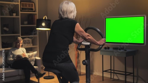 old woman exercise bike watching green screen tv television,healthy lifestyle in isolation elderly lady training work out on stationary bike at home watches chroma key display