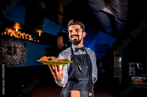 Stylish flunkey carries cooked dish on a black background. photo