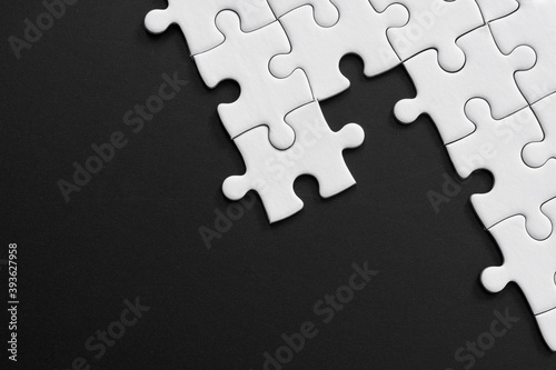 Unfinished white jigsaw puzzle pieces on black background with  copy space