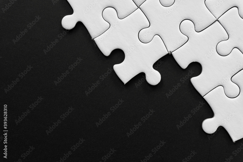 Fototapeta premium Unfinished white jigsaw puzzle pieces on black background with copy space