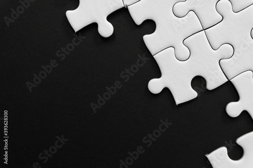 Unfinished white jigsaw puzzle pieces on black background with copy space