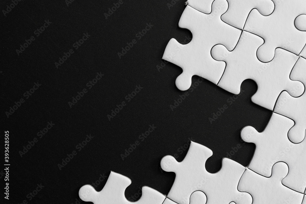 Obraz premium Unfinished white jigsaw puzzle pieces on black background with copy space