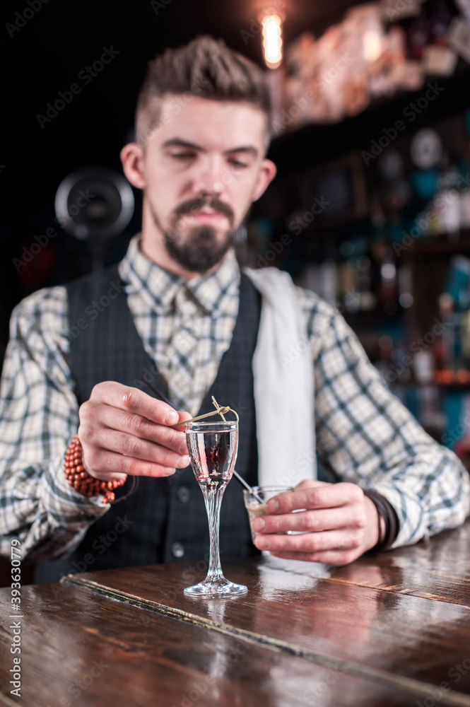 Expert barman mixes a cocktail while standing near the bar counter in bar