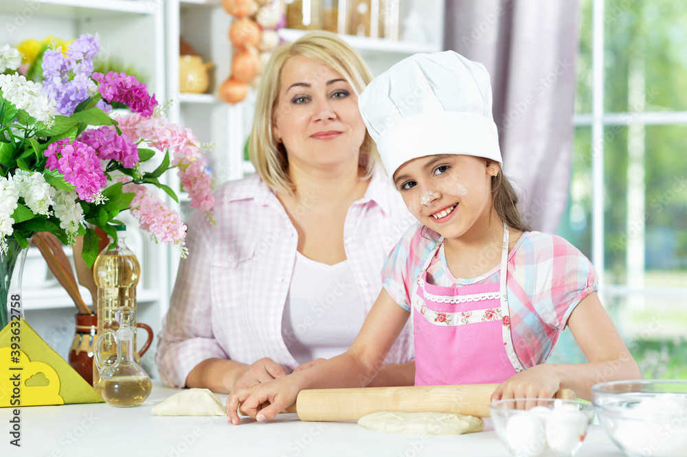 Cute girl in white hat with her mother making dough Cute girl in white hat with her mother making dough