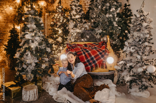 Mother and son have a fun near retro car and Christmas tree during snowfall.