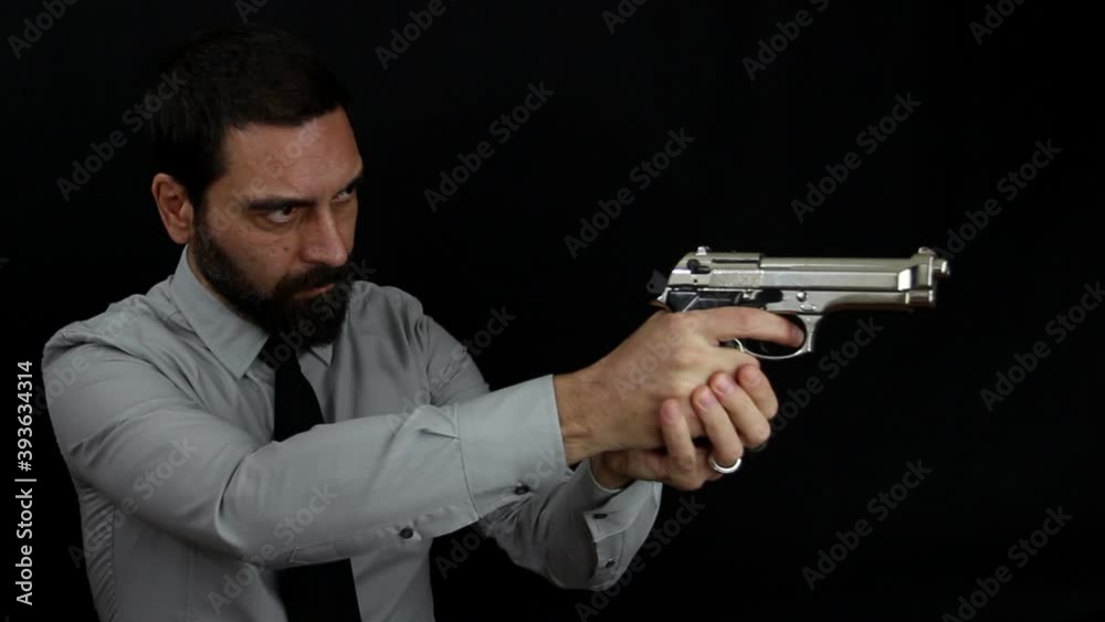 Handsome bearded man in shirt and tie on black background loads the shot in the barrel of his silver pistol and takes aim. Policeman dressed in civilian clothes Handsome bearded man in shirt and tie on black background loads the shot in the barrel of his silver pistol and takes aim. Policeman dressed in civilian clothes