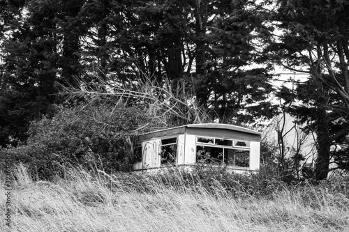 abandoned and broken mobile home trailer falling apart in the tall grass and forest. © Corey