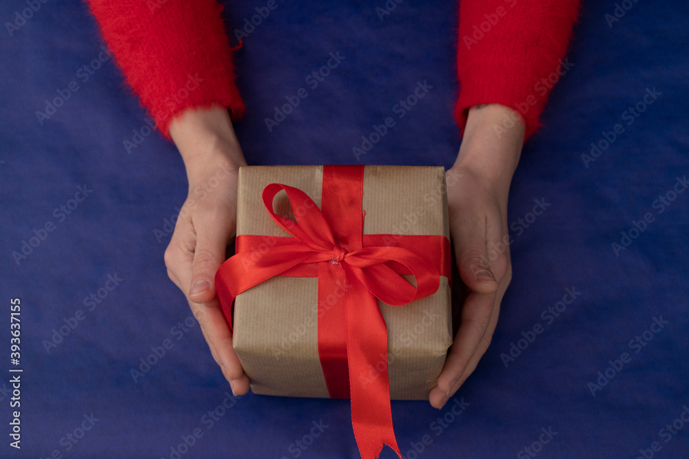 Gift wrapped in craft paper with a wide red ribbon in hands on a blue background. Holidays Gift wrapped in craft paper with a wide red ribbon in hands on a blue background. Holidays