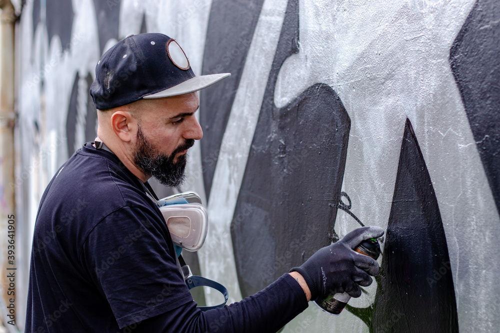 Graffiti artist in action, painting on the wall with aerosol spray ...