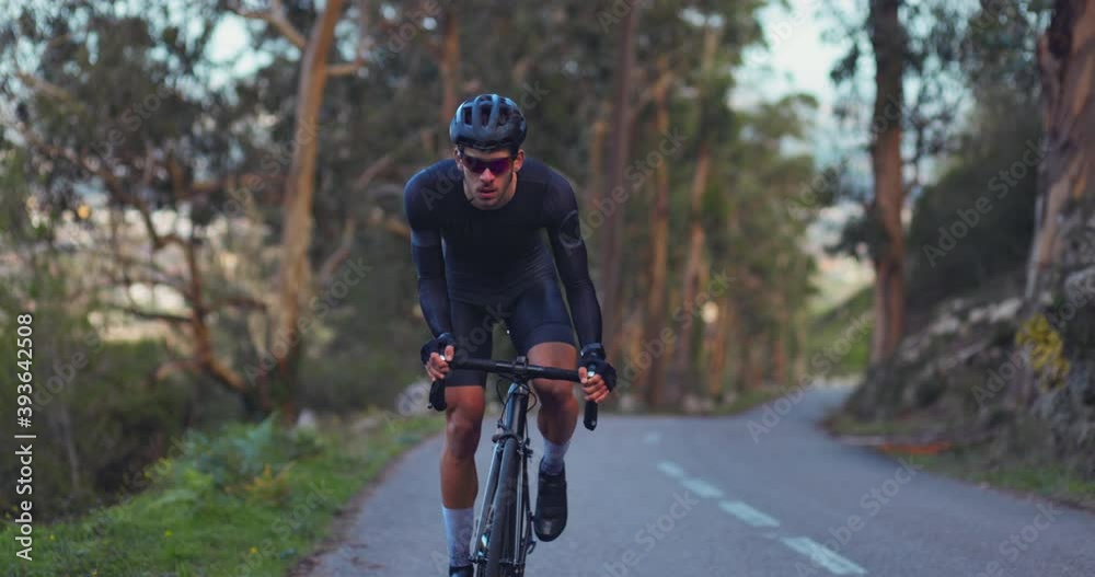 Professional cyclist riding sports bicycle uphill on a forest