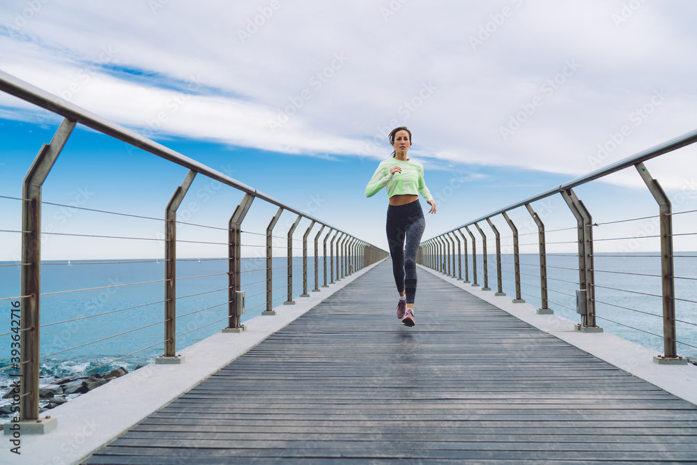 Sportswoman jogging on bridge near sea