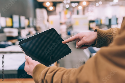 A man in a furniture store holds a tablet in his hand.