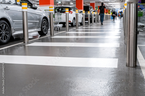 Parking garage underground interior, pedestrian crossing. Illuminated underground car parking interior under modern mall with lots of vehicles and arrows on floor.