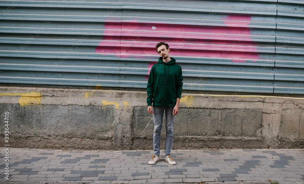 City portrait of charismatic hipster guy wearing green (watercolor) blank hoodie with space for your logo or design. Mockup for print City portrait of charismatic hipster guy wearing green (watercolor) blank hoodie with space for your logo or design. Mockup for print
