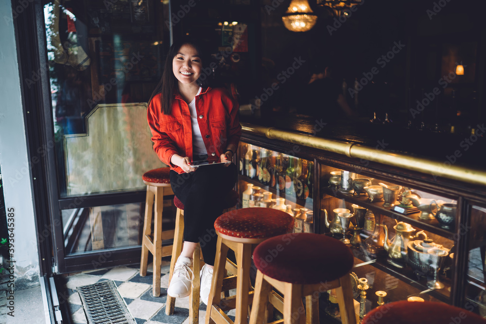 Happy young Asian woman with tablet sitting at bar counter in cafe Happy young Asian woman with tablet sitting at bar counter in cafe